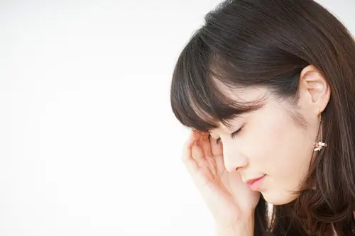 頭痛でこめかみを抑える女性イメージ